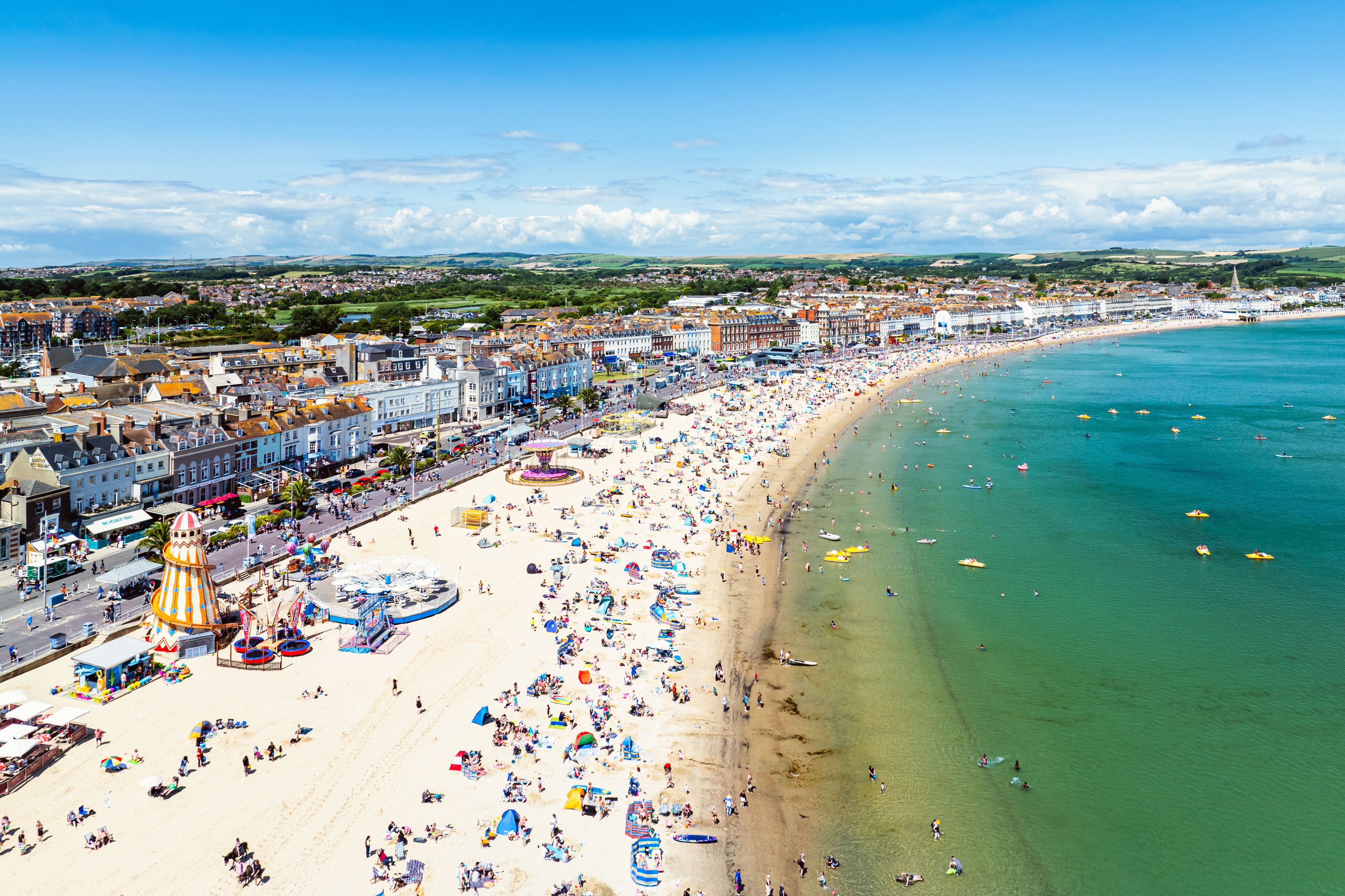A coastal cityscape with a wide beach, clear blue waters, and a historic town center.