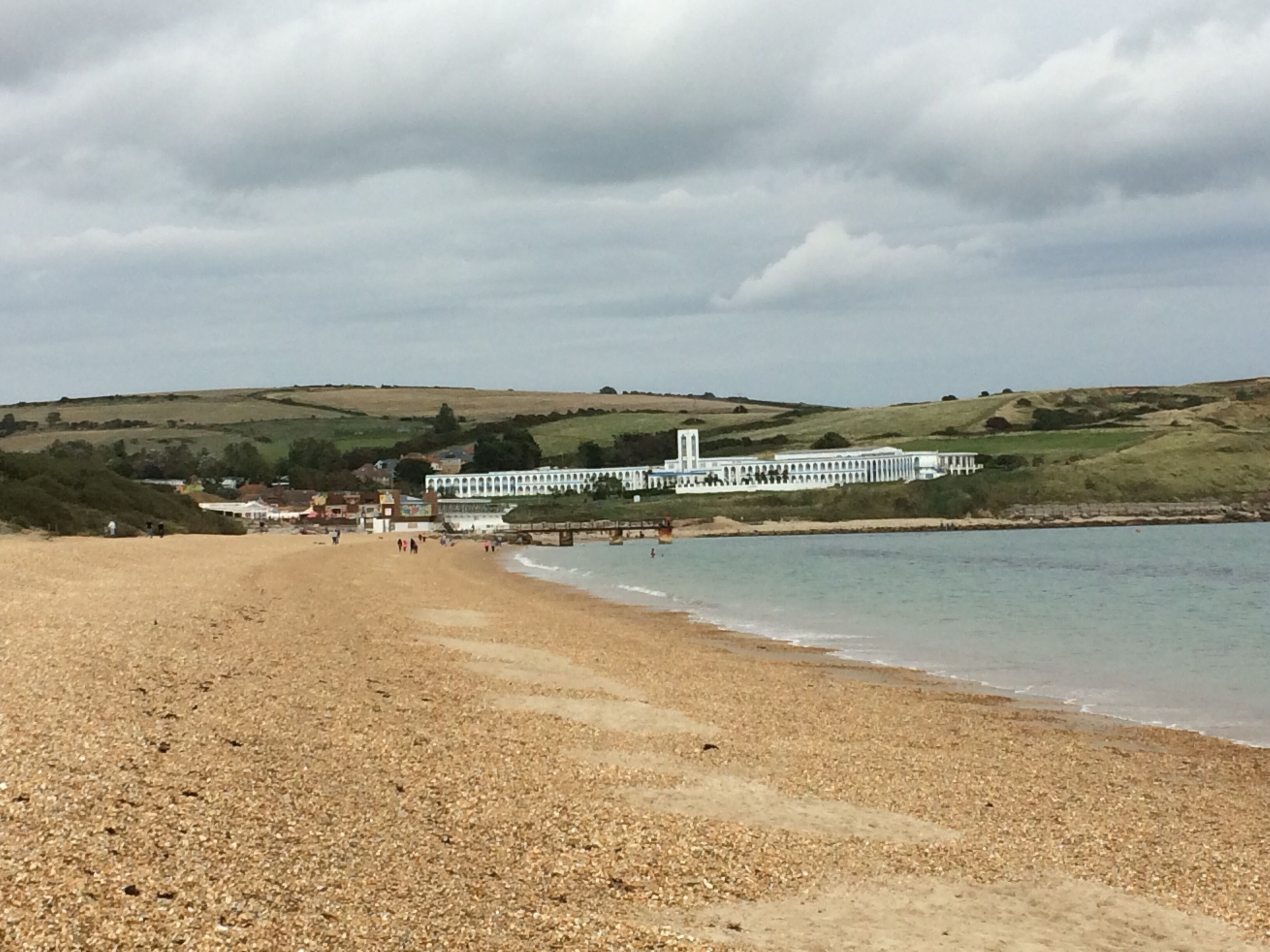 A pebbled beach with a white building and a bridge in the background.