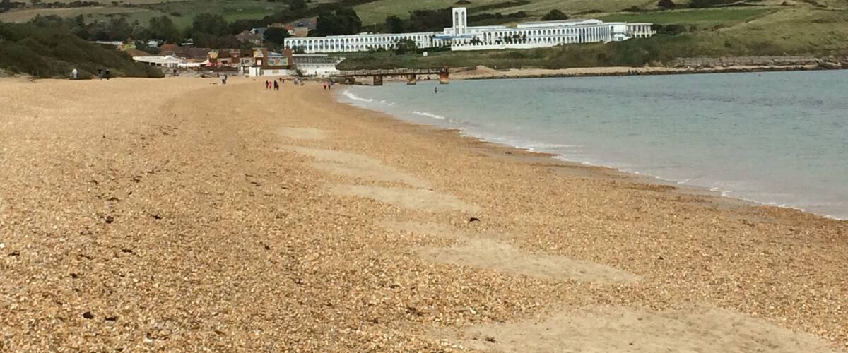 A pebbled beach with a white building and a bridge in the background.