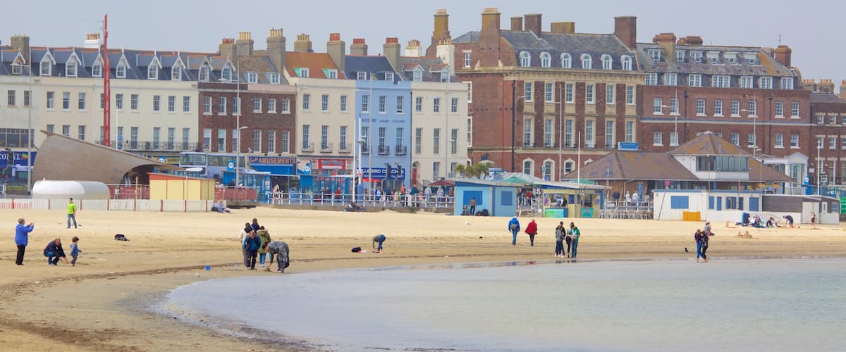 A beach with people walking and playing, and a row of colorful buildings in the background.