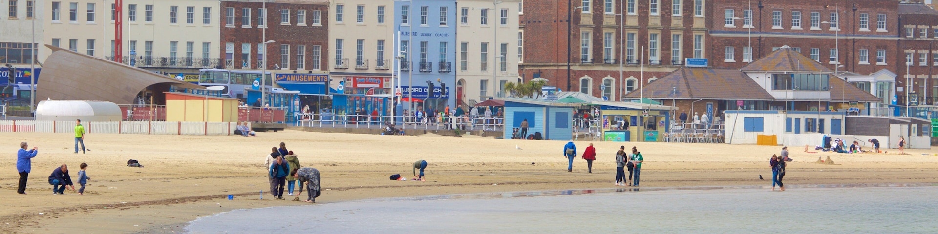A beach with people walking and playing, and a row of colorful buildings in the background.