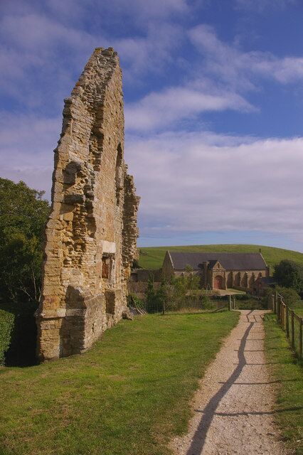 A stone ruin with a pathway leading to a building in a rural setting.