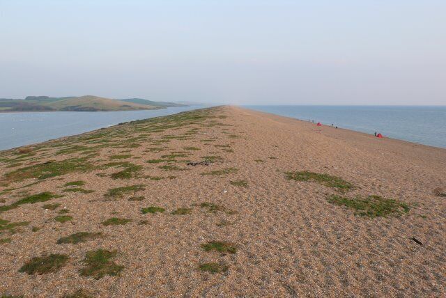 A sandy beach with sparse vegetation and a calm sea in the background.