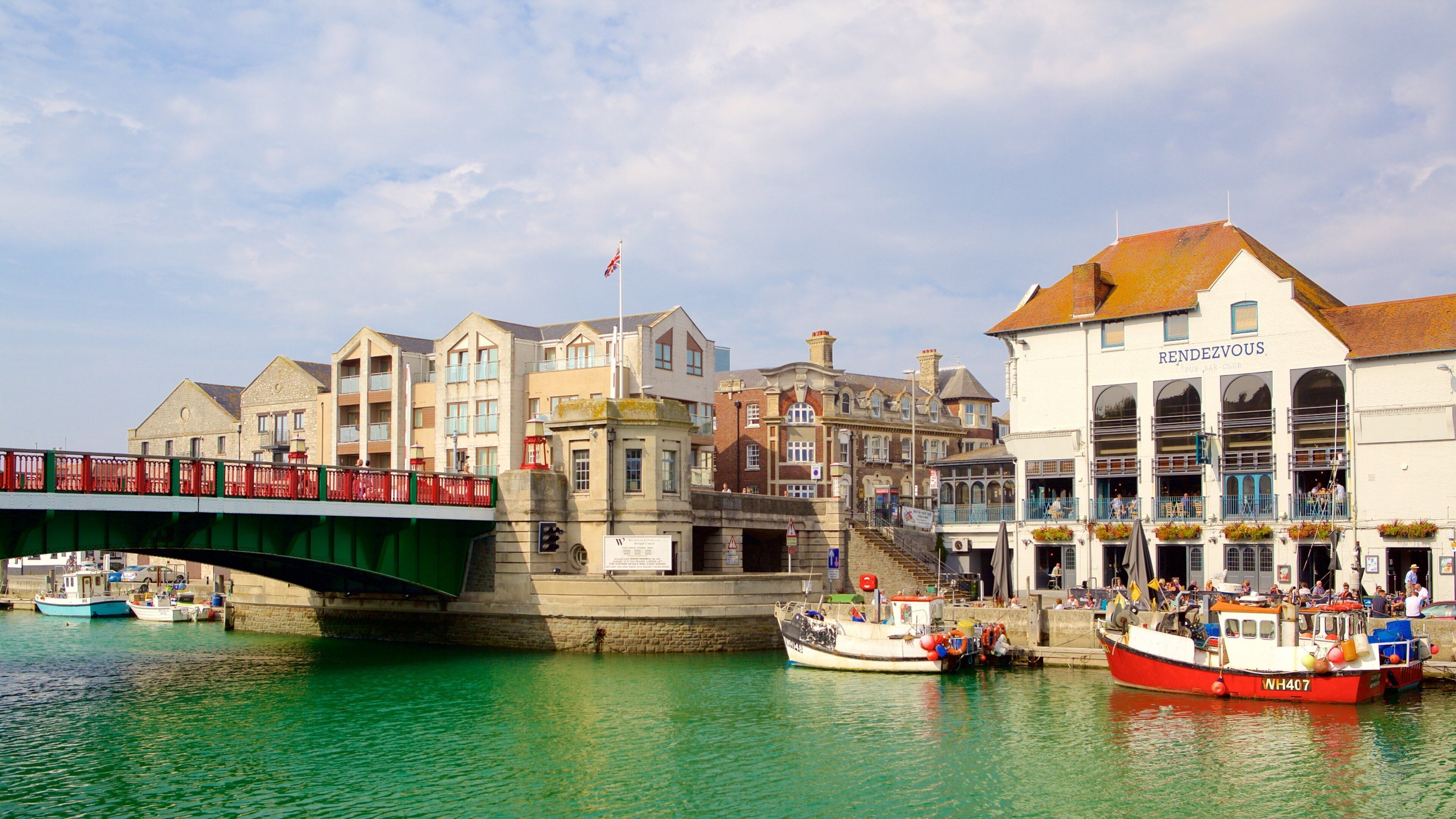 A bridge over a canal with boats docked nearby and buildings in the background.