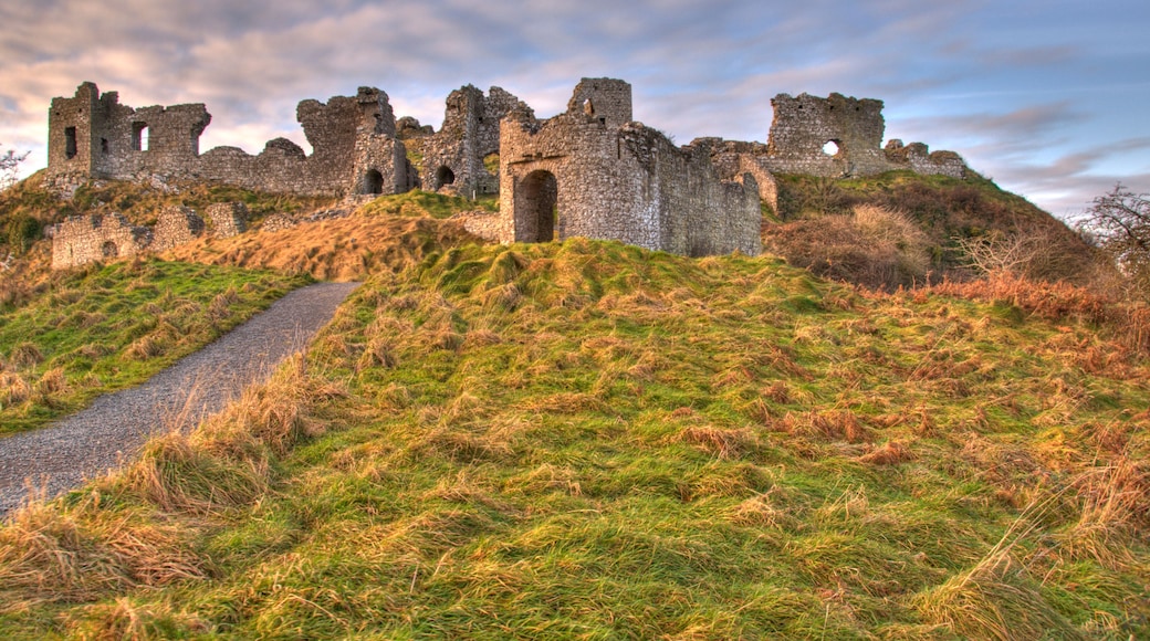 A historic stone castle ruins on a grassy hill with a gravel path leading up to it.