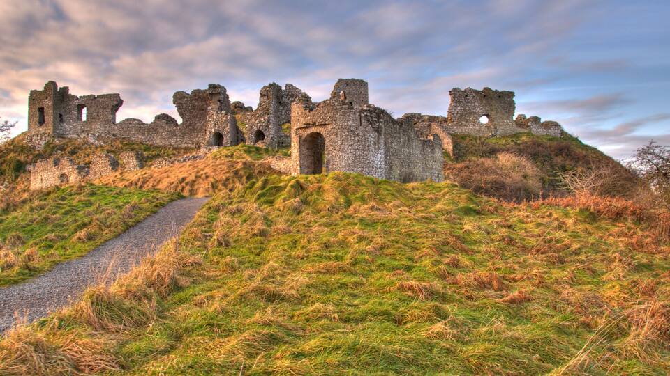 A historic stone castle ruins on a grassy hill with a gravel path leading up to it.