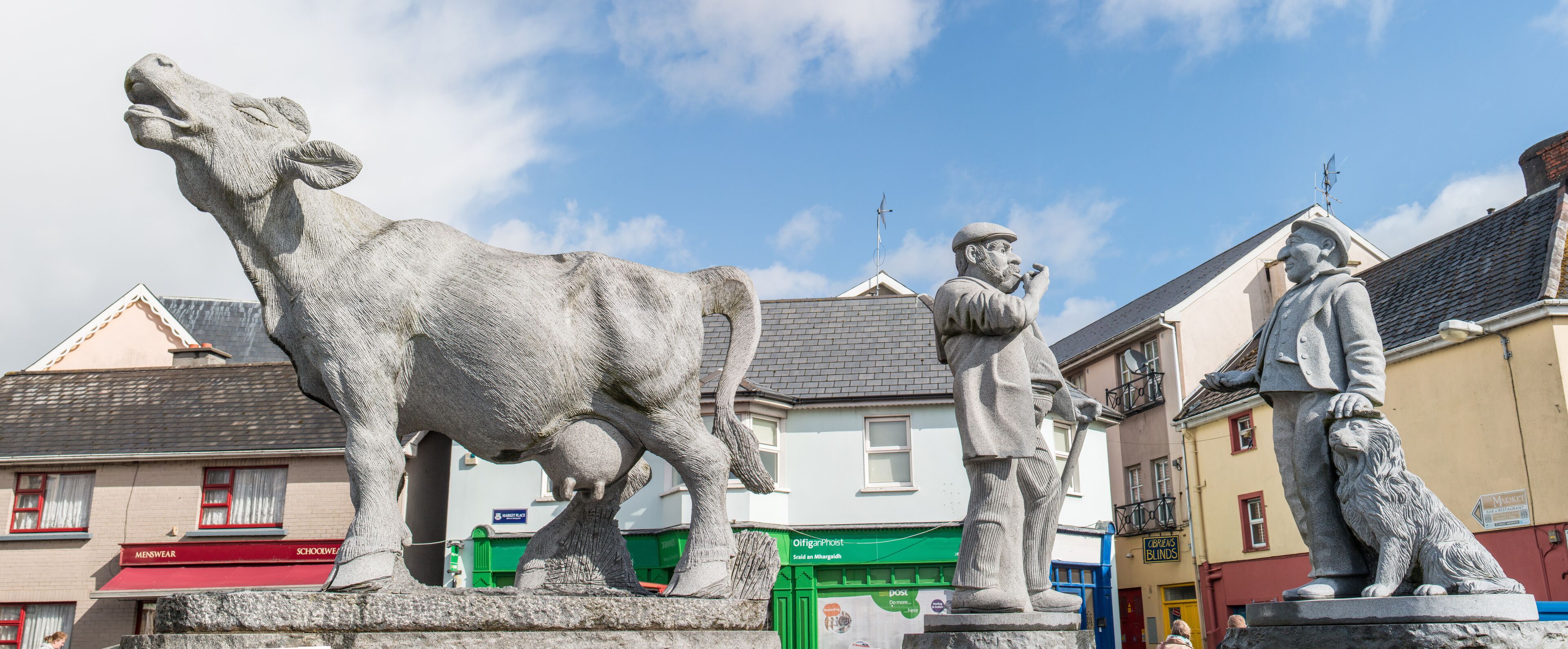 A statue of a cow, a man with a pipe, and a lion statue in an urban setting.