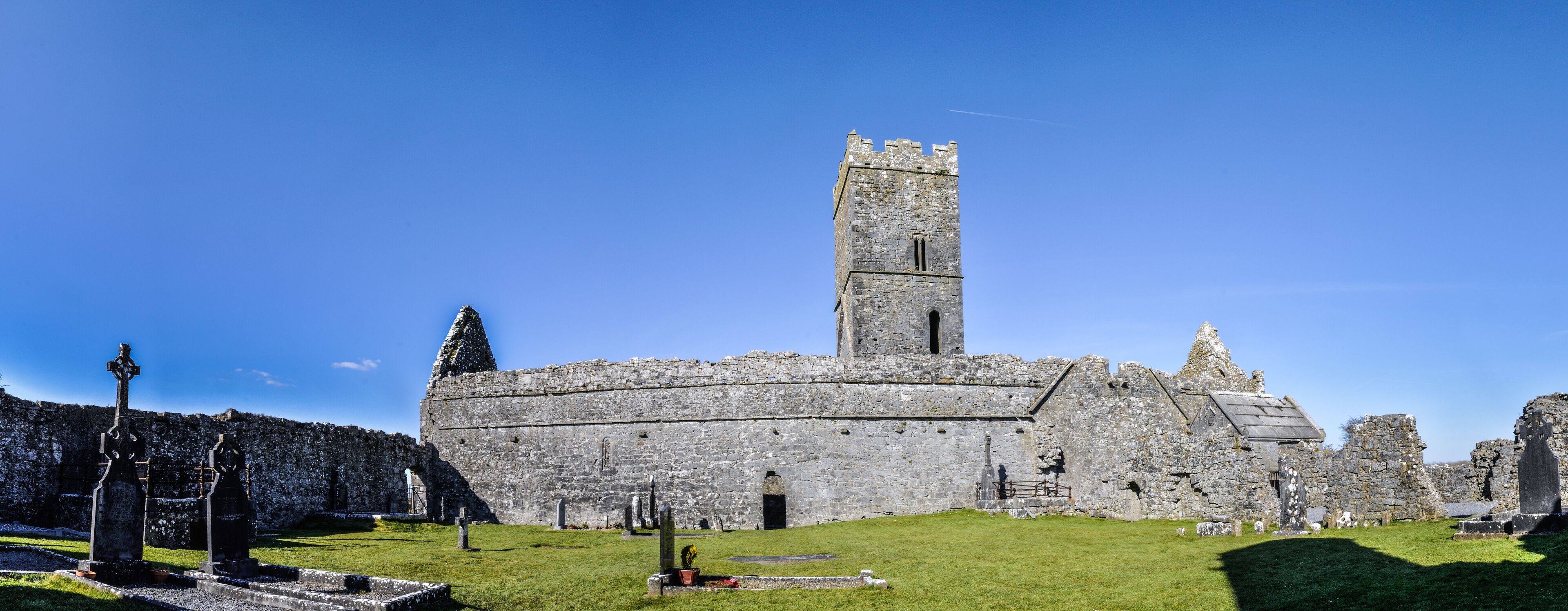 A historic stone castle with a tall tower, surrounded by a grassy area with several standing crosses.