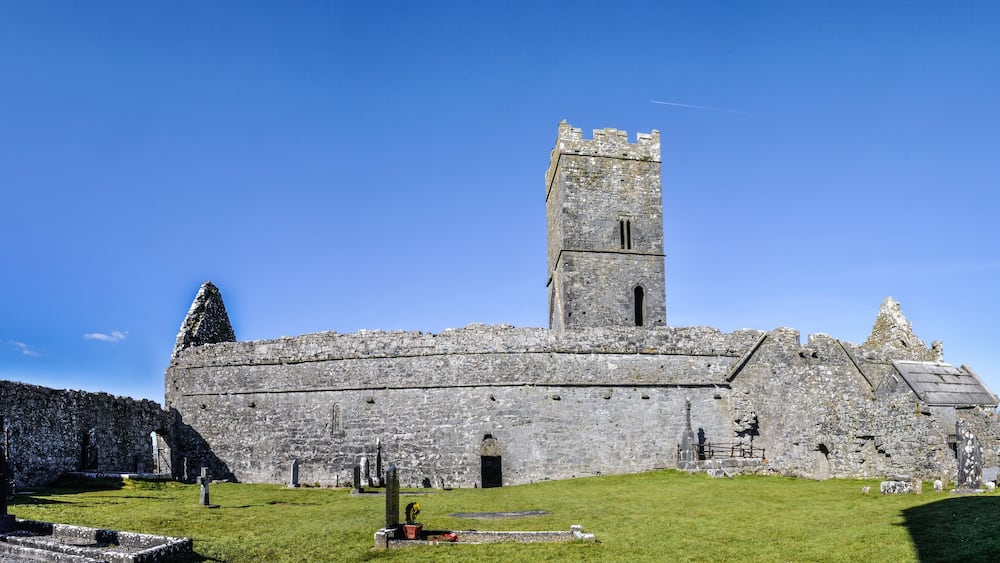 A historic stone castle with a tall tower, surrounded by a grassy area with several standing crosses.