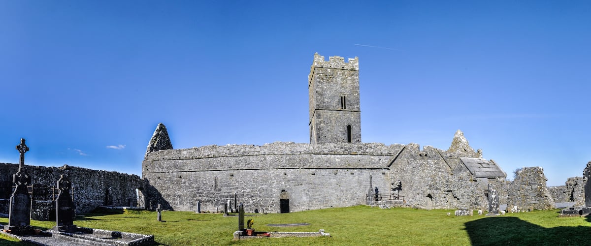 A historic stone castle with a tall tower, surrounded by a grassy area with several standing crosses.
