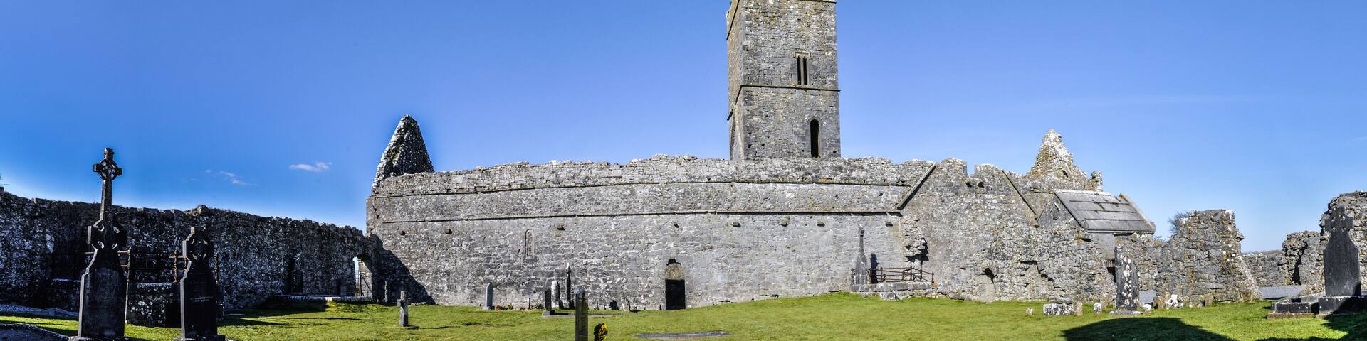 A historic stone castle with a tall tower, surrounded by a grassy area with several standing crosses.