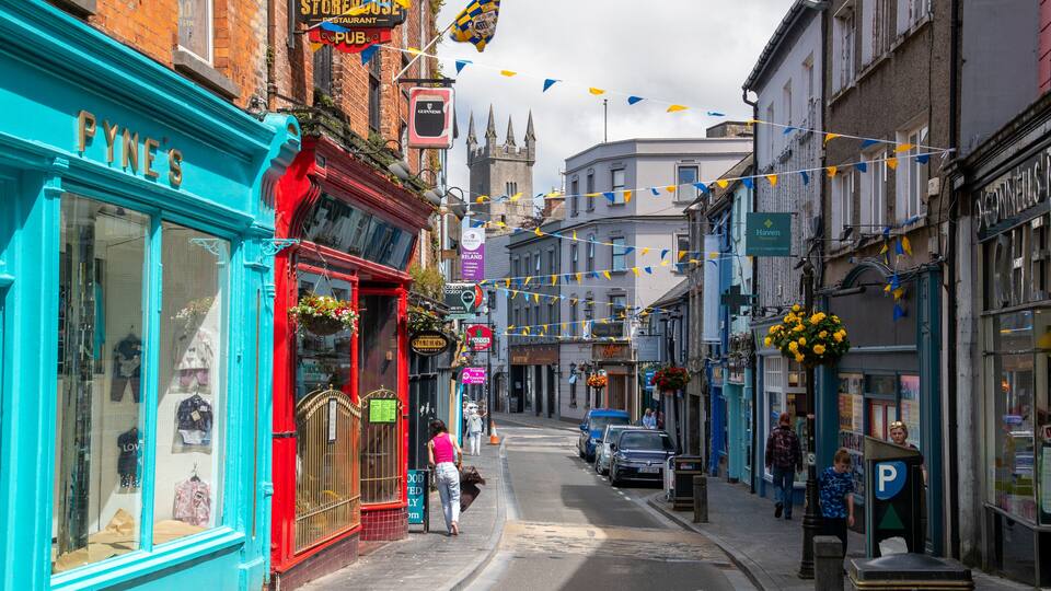 A narrow street lined with colorful shops, including a blue storefront and a red building with hanging flower baskets.