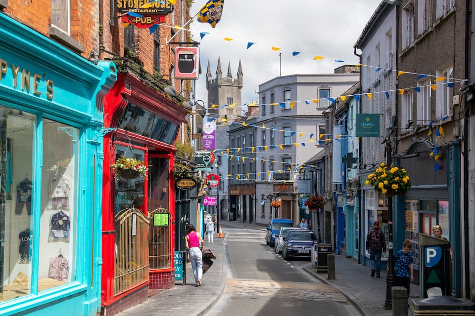 A narrow street lined with colorful shops, including a blue storefront and a red building with hanging flower baskets.