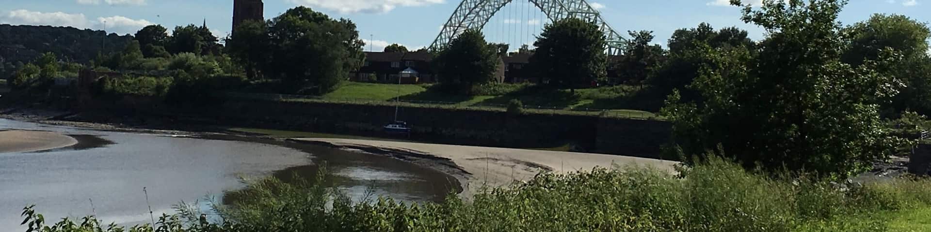 A coastal landscape with a large green bridge, a river, and a castle in the background.