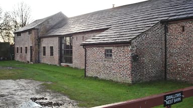 Um edifício de tijolos com telhado inclinado e uma placa com a inscrição 'Swallows Nest Barn'.