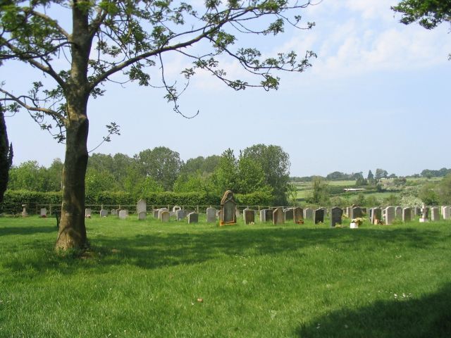 A cemetery with headstones and a large tree in the foreground.
