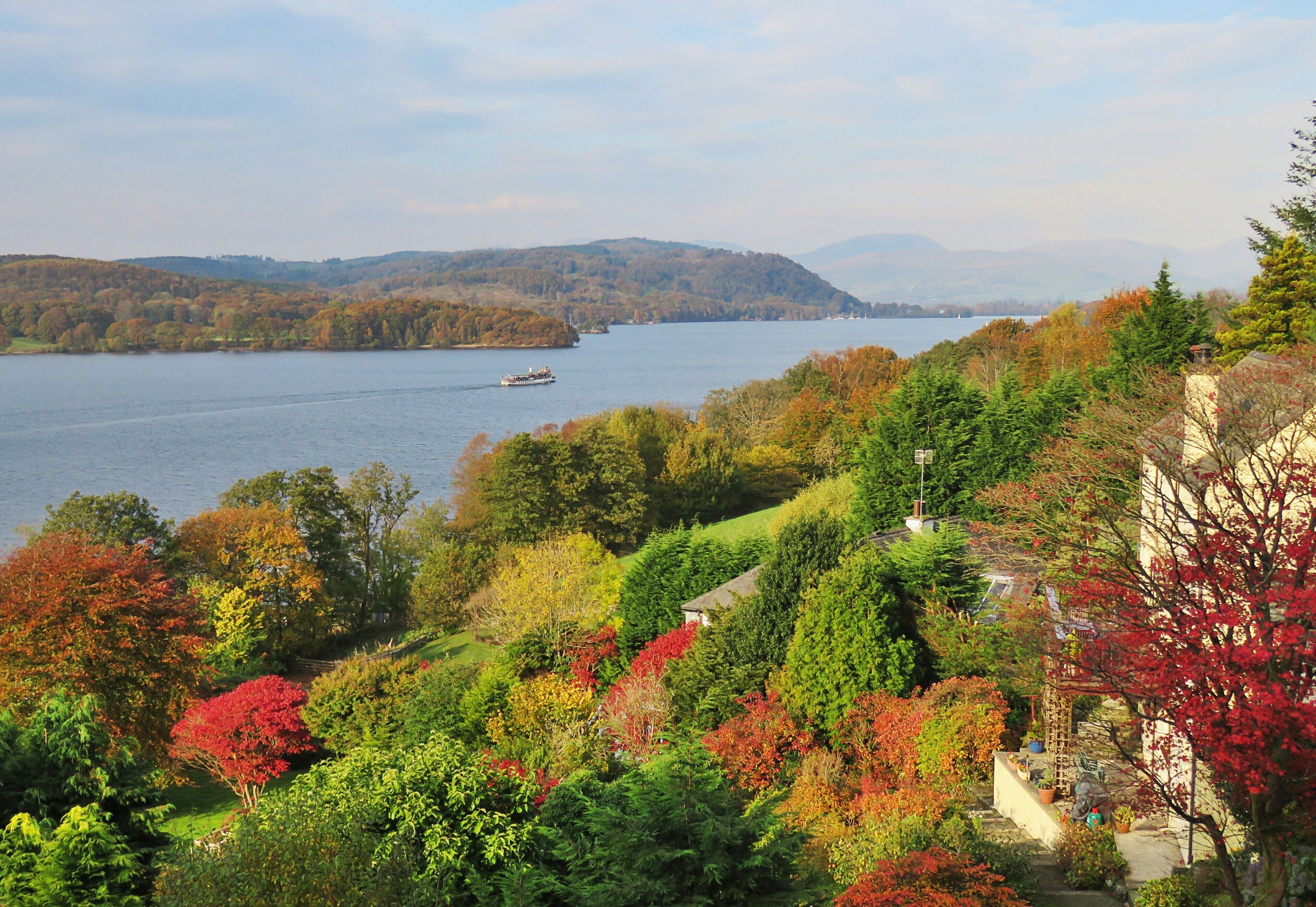 A river with a boat, surrounded by autumn-colored trees and hills in the background.