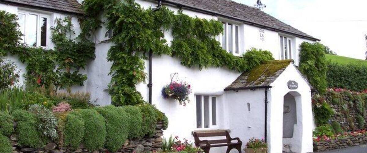 A white building with ivy, a bench, and a stone wall.
