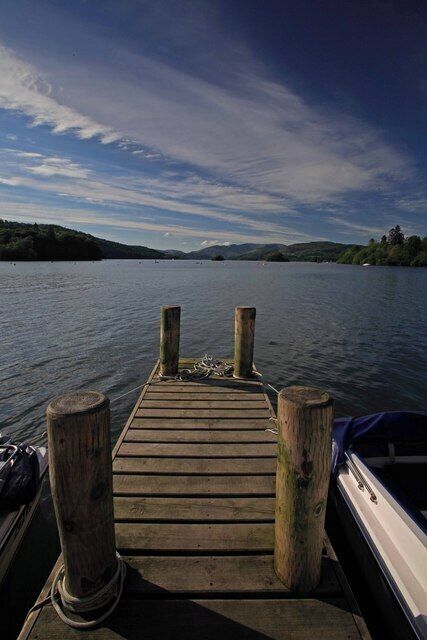 A wooden dock extending into calm water with hills in the background.