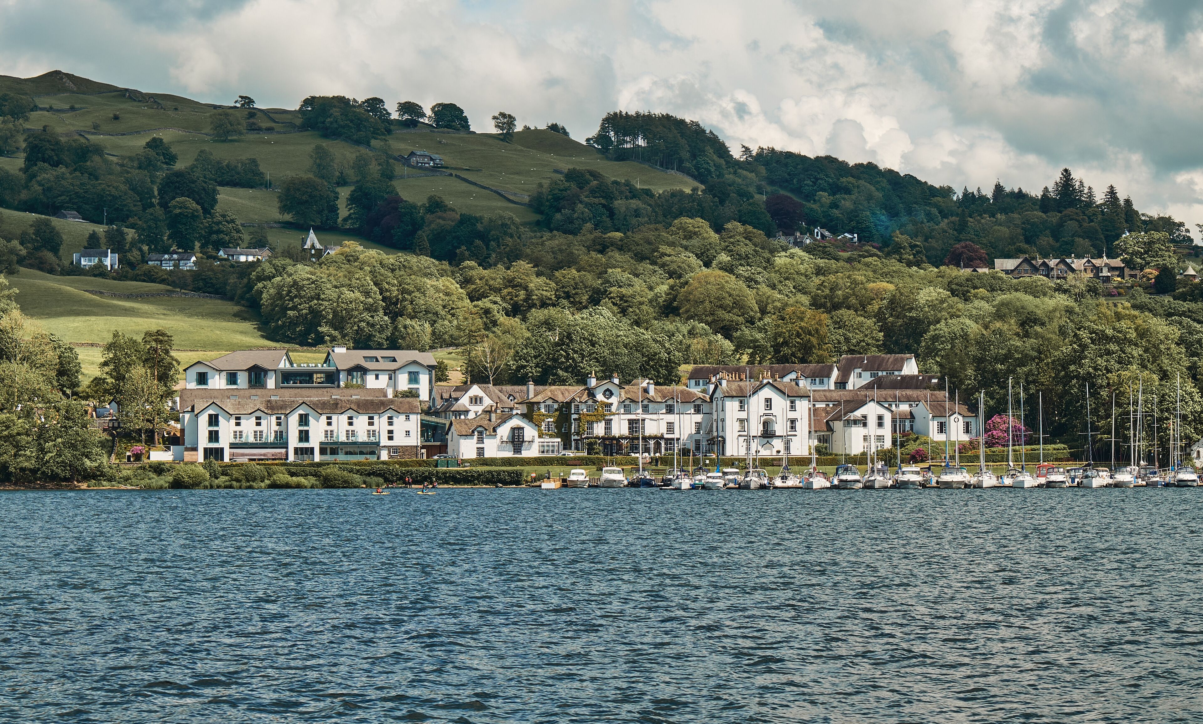 Un pueblo a orillas del lago con casas blancas, un puerto deportivo y colinas onduladas al fondo.