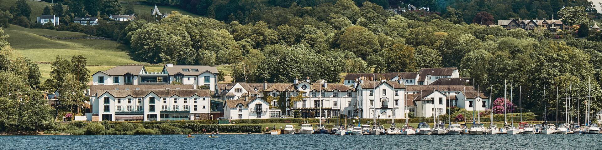 A lakeside village with white houses, a marina, and rolling hills in the background.