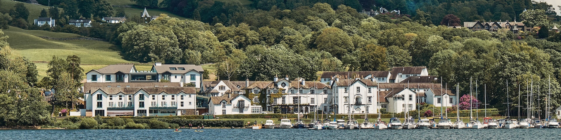 Un pueblo a orillas del lago con casas blancas, un puerto deportivo y colinas onduladas al fondo.