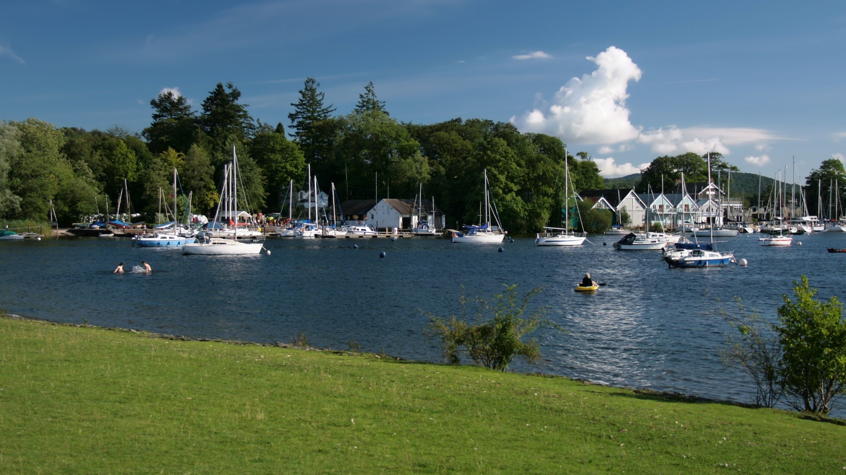 A lake with boats, a grassy shore, and trees in the background.