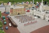 Een gedetailleerd model van een historisch stadsplein met miniatuurgebouwen, een rode dubbeldekkerbus en een regiment bewakers.