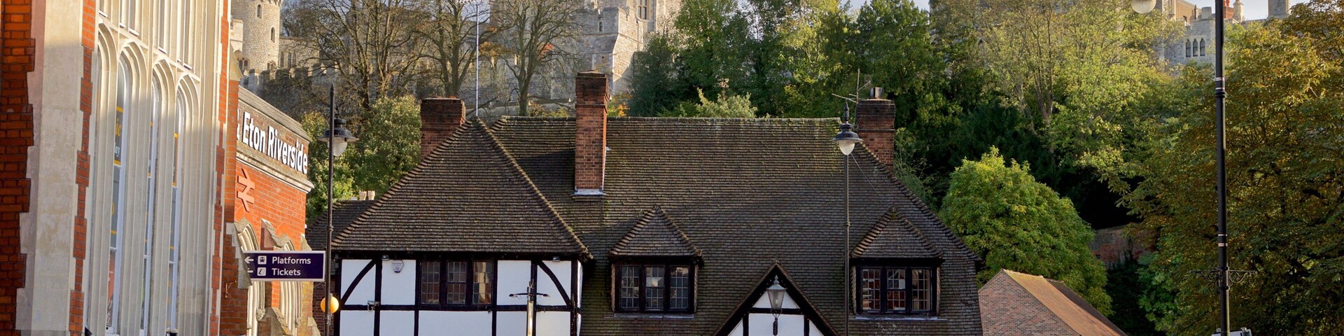 Um edifício histórico com arquitetura em estilo Tudor, um pub chamado 'The Royal Oak' e um castelo ao fundo.