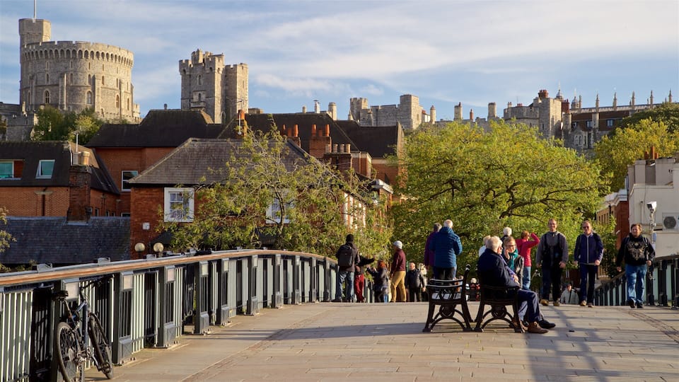 A historic stone castle with towers and a bridge with people walking and sitting.