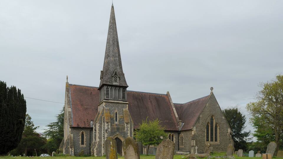 A church with a tall spire, stone walls, and a graveyard with headstones.