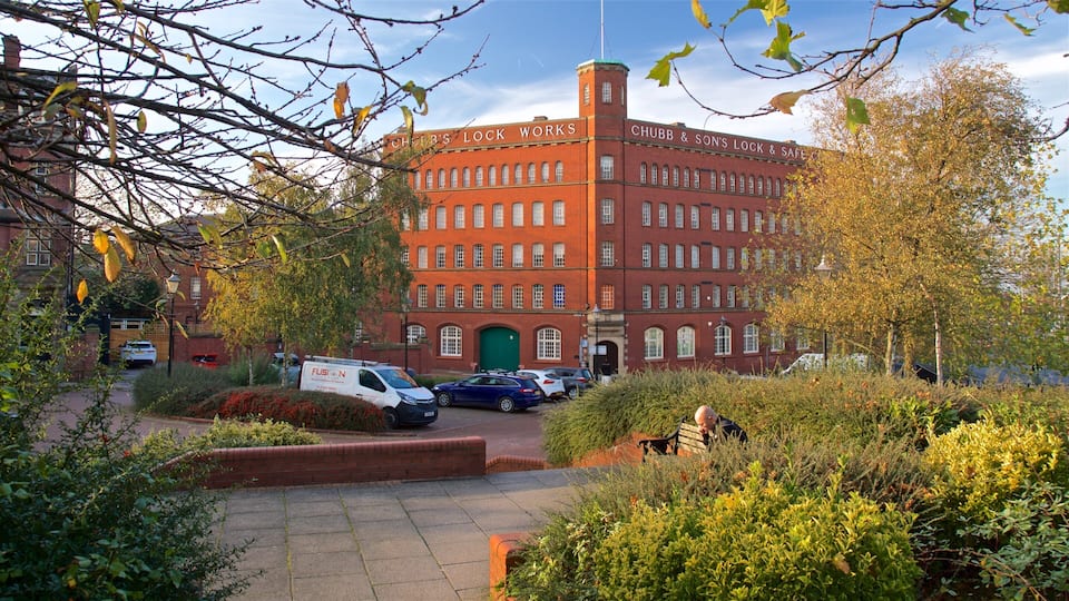 A red brick building with multiple windows and a green door, surrounded by trees and parked cars.