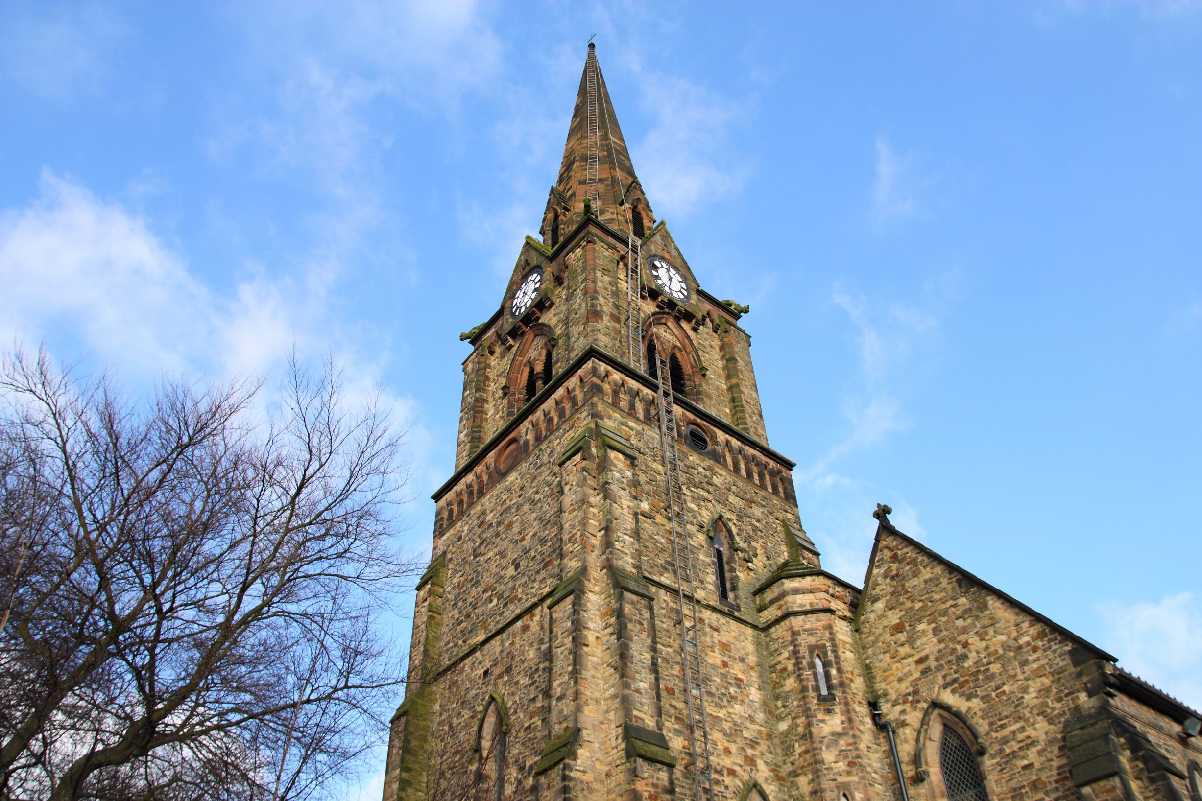 A tall church tower with a pointed spire and two large clocks.