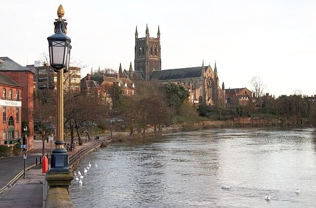A river with swans, a lamp post, and a historic building in the background.