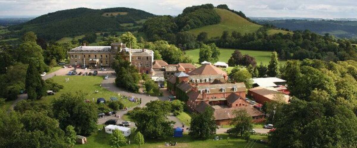 A large estate with multiple buildings, surrounded by lush green hills and a clear sky.