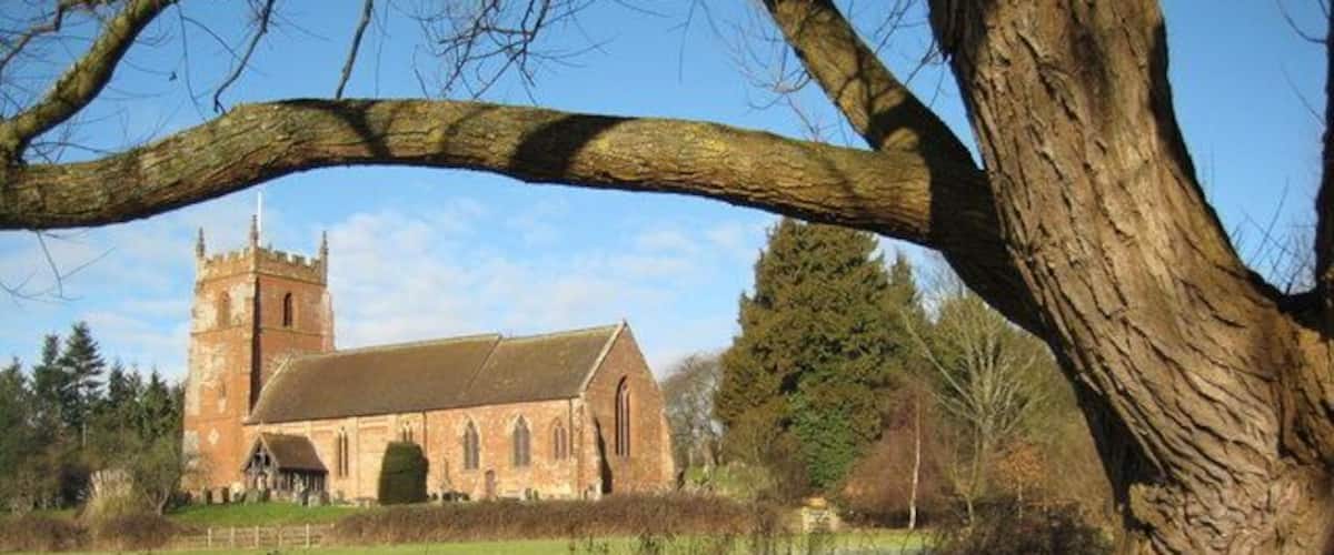 A church with a tower and a large tree in the foreground.