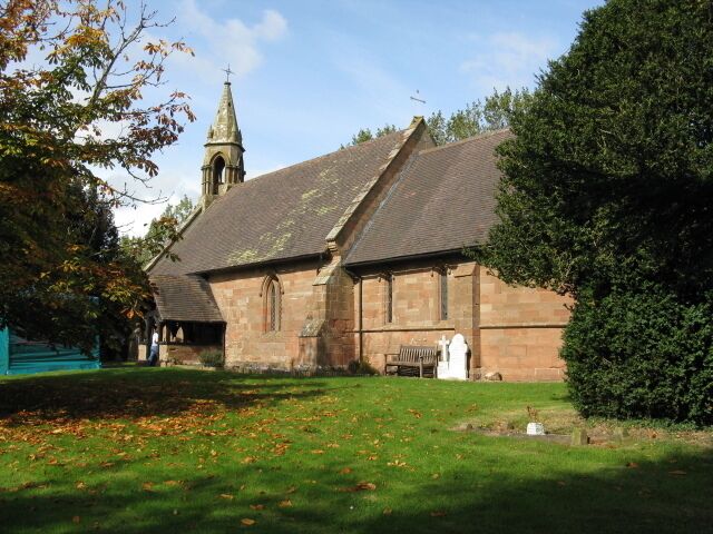 A church with a steeple, a grassy lawn, and a bench.