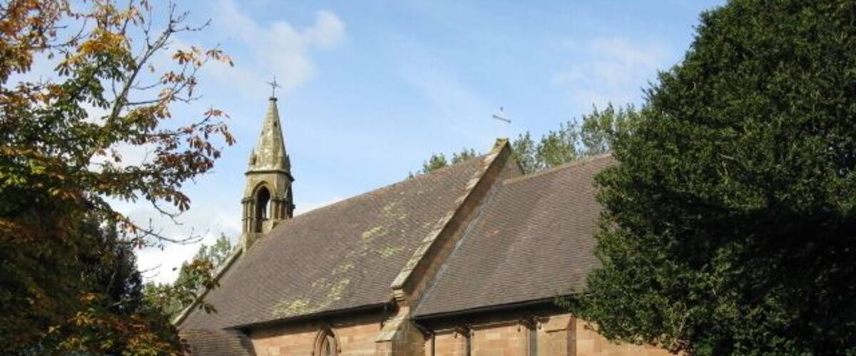 A church with a steeple, a grassy lawn, and a bench.