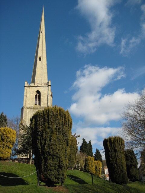 A church with a tall spire, surrounded by neatly trimmed hedges and trees.