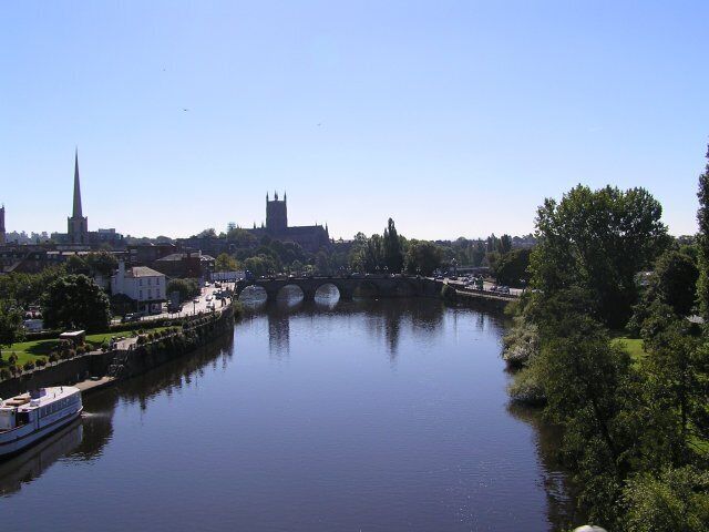 A river with a bridge, a boat, and buildings including a tall spire and a church.