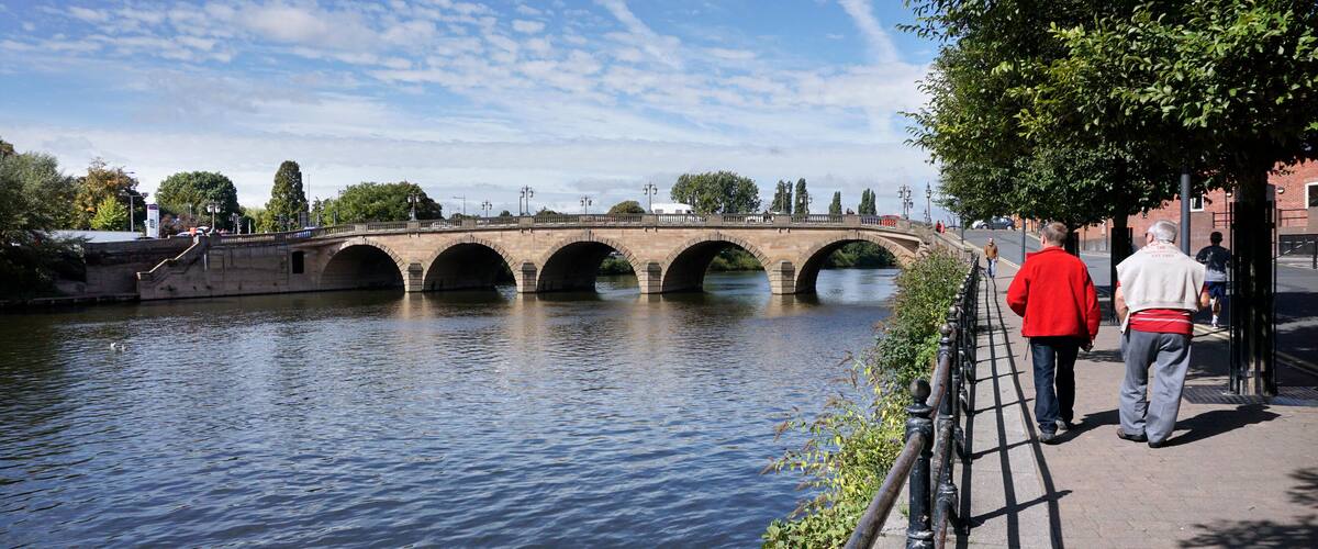 A stone bridge over a river with pedestrians on the sidewalk.