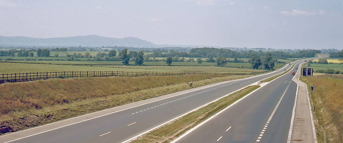 A multi-lane highway with grassy fields and distant mountains.