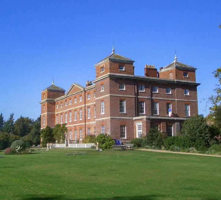 A large, red brick building with multiple towers and a well-maintained lawn in front.