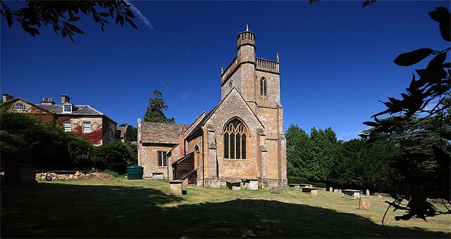 A historic church with a tall tower and arched windows, surrounded by a cemetery and greenery.