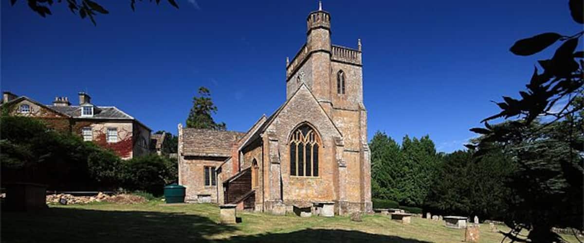 A historic church with a tall tower and arched windows, surrounded by a cemetery and greenery.