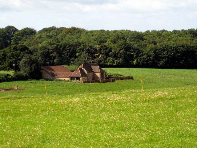 Converted barns and Moor's Plantation Looking from the top of Lodge Hill through the electric sheep fence to the barns and wood behind. The road runs to Pen Cross to the left of the buildings.