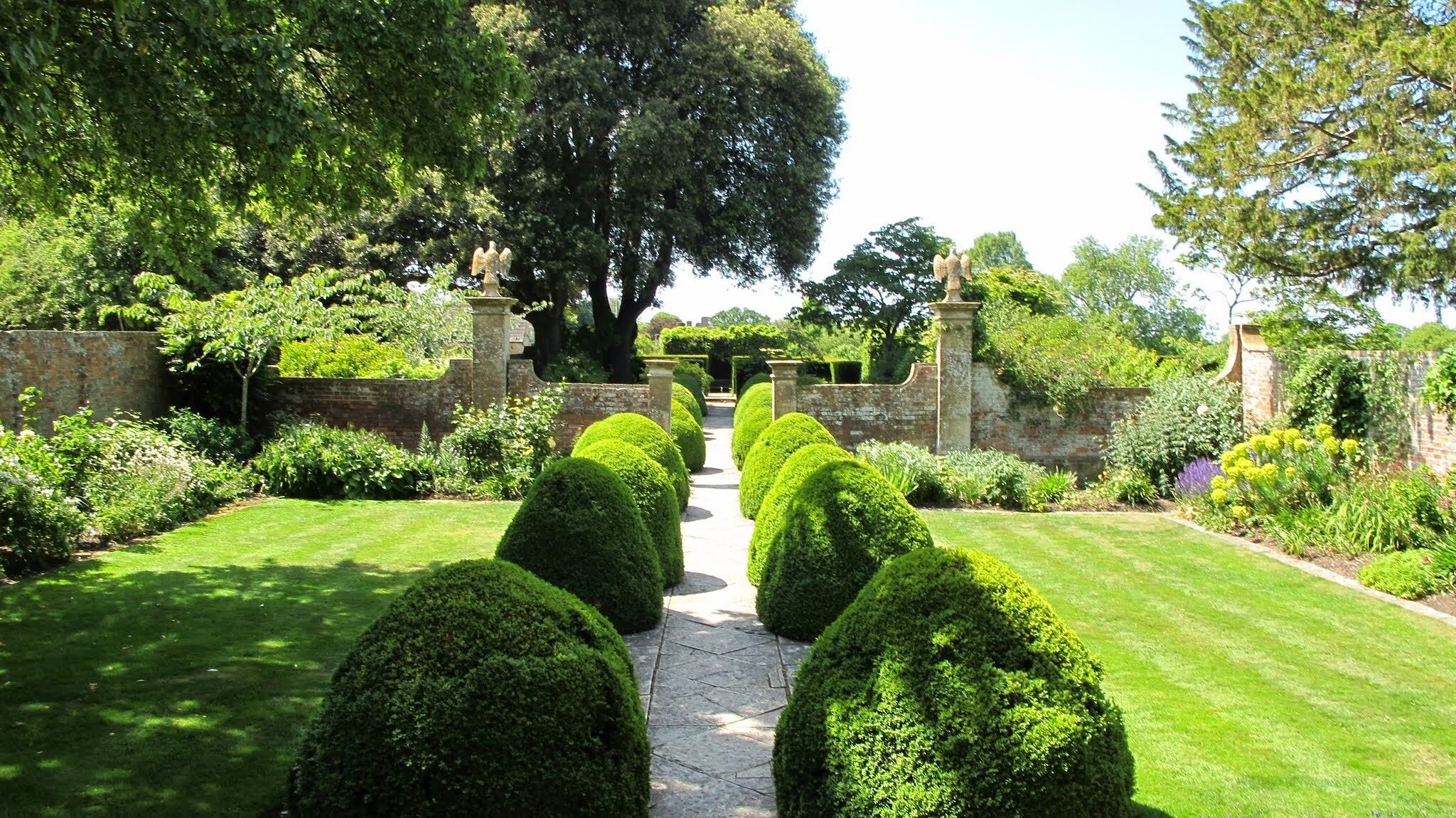 Un jardín formal con setos bien cuidados, un camino central y estatuas clásicas.