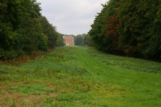 A grassy path leading to a red brick building surrounded by trees.