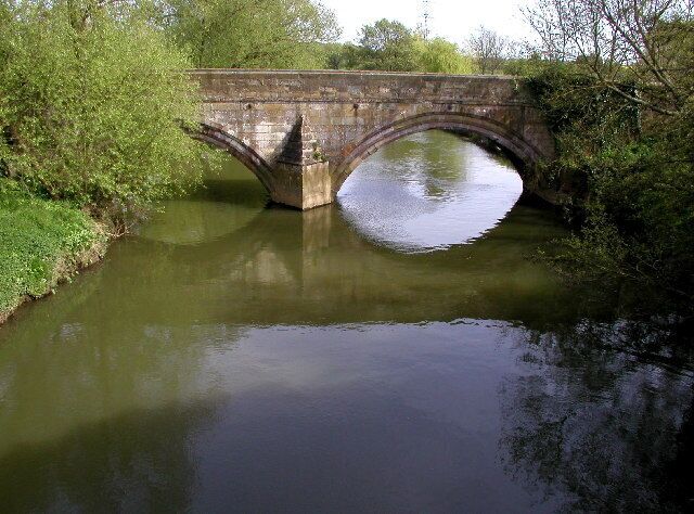 A stone bridge over a calm river surrounded by greenery.