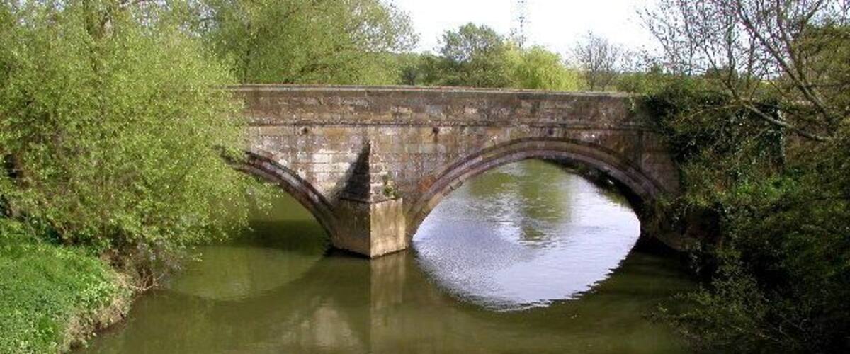 A stone bridge over a calm river surrounded by greenery.